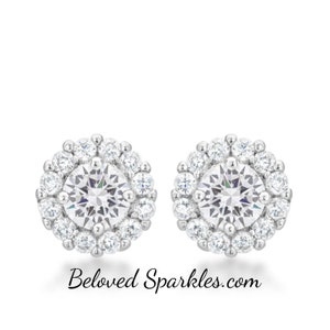 May include: A pair of silver stud earrings with a round, clear, sparkling stone surrounded by a halo of smaller stones.