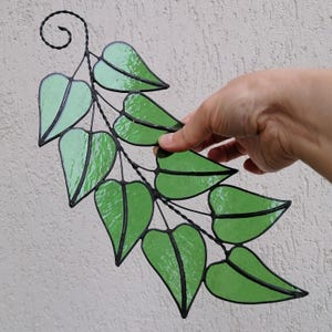 May include: A stained glass leaf garland with a vine design. The leaves are green with a light green gradient and are connected by black wire.