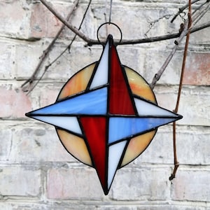 Op de afbeelding: Een gebrandschilderd zonnenvanger in de vorm van een vierpuntige ster. De ster is gemaakt van rood, blauw, wit en geel glas. De zonnenvanger hangt aan een tak.