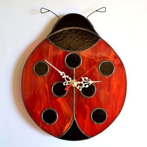 May include: A red and black stained glass ladybug clock with black dots and a white clock face with black hands.
