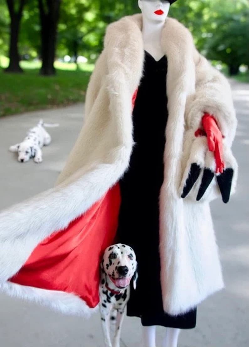 Puede incluir: Una mujer con un abrigo de piel blanco con forro rojo y un vestido negro. Lleva un cachorro d&aacute;lmata en brazos. Otro cachorro d&aacute;lmata est&aacute; tumbado en el suelo en el fondo.