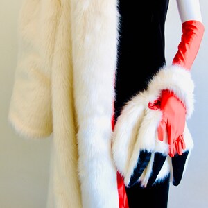 Puede incluir: Un abrigo de piel blanco con forro rojo y un vestido de terciopelo negro. El abrigo est&aacute; drapeado sobre los hombros y el vestido es sin mangas. La persona lleva guantes rojos.