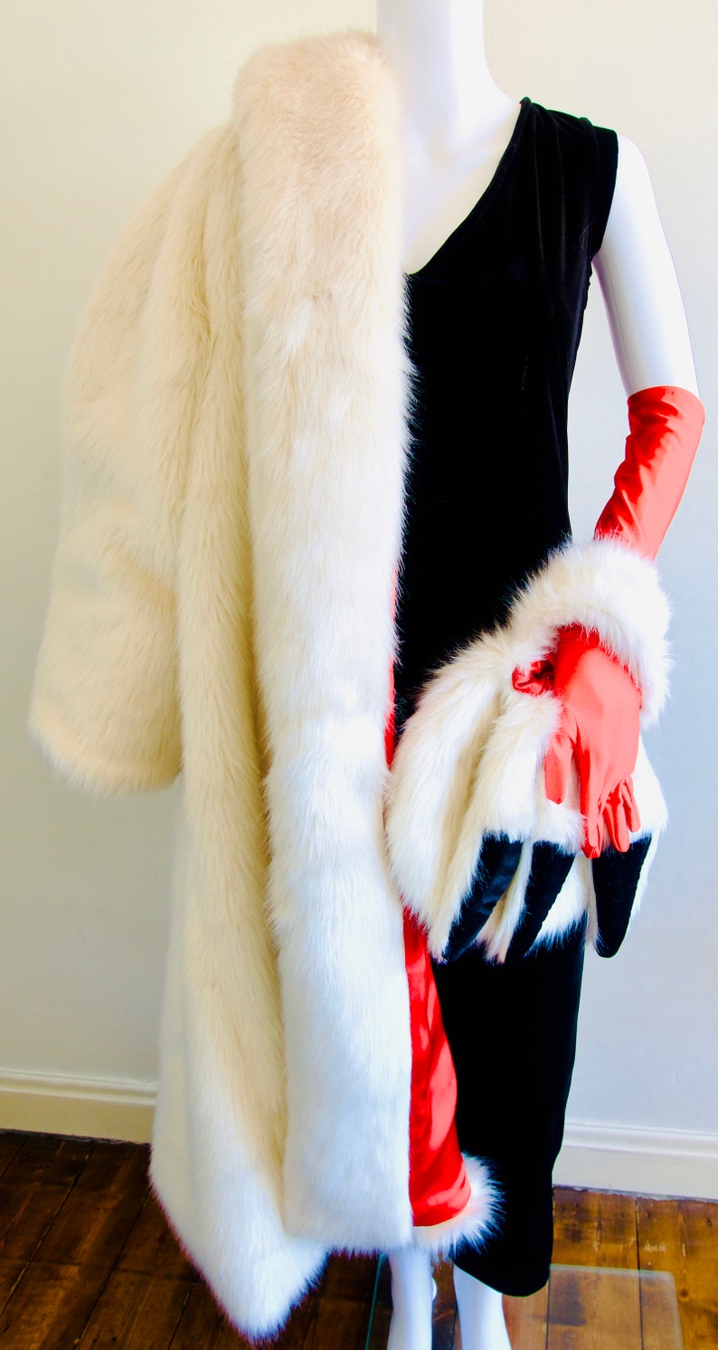 Puede incluir: Un abrigo de piel blanco con forro rojo y un vestido de terciopelo negro. El abrigo est&aacute; drapeado sobre los hombros y el vestido es sin mangas. La persona lleva guantes rojos.