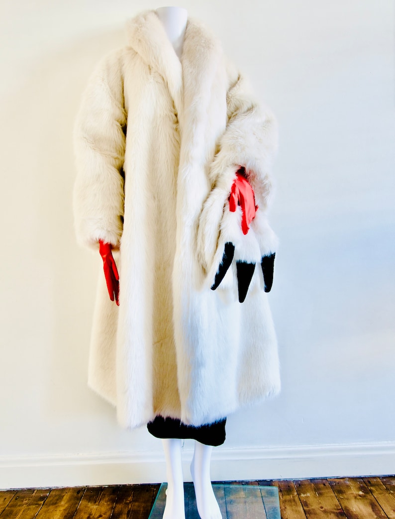 Puede incluir: Un abrigo largo de piel sint&eacute;tica blanca con cuello. El abrigo est&aacute; en un maniqu&iacute; con guantes rojos. El maniqu&iacute; est&aacute; de pie sobre un suelo de madera.