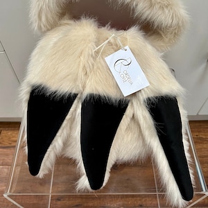 Puede incluir: Una chaqueta con capucha de piel sint&eacute;tica blanca con orejas de piel sint&eacute;tica negra. La chaqueta tiene una etiqueta que dice "Ordelia Oye".