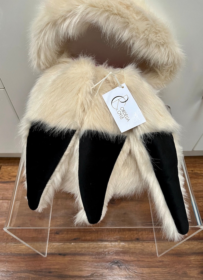 Puede incluir: Una chaqueta con capucha de piel sint&eacute;tica blanca con orejas de piel sint&eacute;tica negra. La chaqueta tiene una etiqueta que dice "Ordelia Oye".
