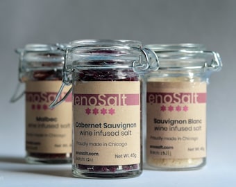 May include: Three glass jars with brown labels and silver lids containing wine infused salt. The labels read "enoSalt" and list the wine varietals: Malbec, Cabernet Sauvignon, and Sauvignon Blanc. Each jar contains 4.5 oz of salt.