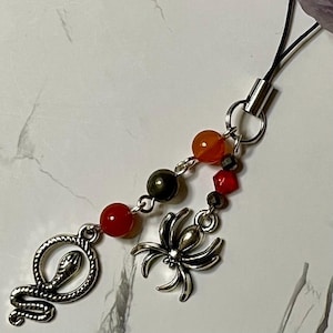 Peut inclure: Un porte-clés de téléphone en argent avec un serpent, une araignée et des perles de cornaline.