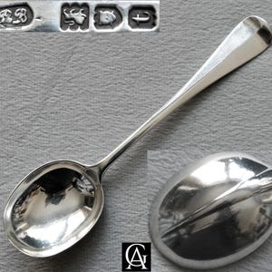 May include: A polished silver spoon with a smooth, rounded bowl and a slender handle. The top left corner shows a close-up of four distinct hallmarks, including the letters RB, a lion passant, a leopard head, and the lowercase letter t.