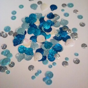 May include: Assortment of blue and white iridescent sequins in various shapes, including circles, ovals, and seashells.