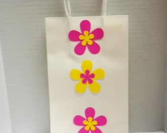 May include: White paper gift bag with three pink and yellow paper flowers. The flowers are in a vertical line down the center of the bag.