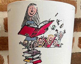 May include: A white lampshade with a whimsical illustration of a woman reading to children. The shade has the text "Don't you ever stop reading?" and sits on a silver-colored metal base.