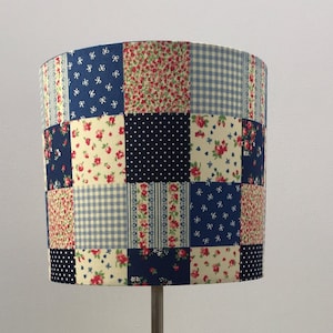 May include: A patchwork lampshade featuring floral, polka dot, and gingham patterns in blue, red, and cream. The lampshade is mounted on a silver-coloured metal lamp base.