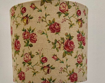 May include: A vintage-style table lamp with a cylindrical lampshade. The shade is covered in a floral pattern of red roses and green leaves on a beige background. The lamp has a silver metal base and stem.