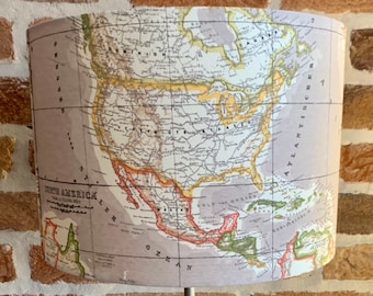 May include: A table lamp with a cylindrical lampshade featuring a vintage map of North America. The lamp has a silver-colored base and stem. The lampshade displays the map in muted tones of beige, green, and brown.