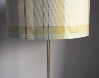 May include: A table lamp with a cylindrical lampshade featuring a plaid pattern in shades of gray, yellow, and cream. The lamp has a silver-colored metal base and stem. The lampshade is approximately 10 inches in diameter.