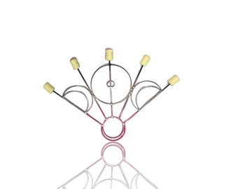May include: A silver fire fan with five wicks. The fan has a circular design with a pink centre and is reflected below. The wicks are yellow and cylindrical.