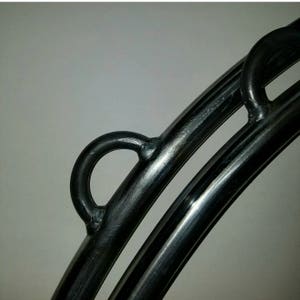 May include: Close-up of a black metal hoop with two welded loops. The hoop is made of thick, round metal and has a smooth, polished finish.