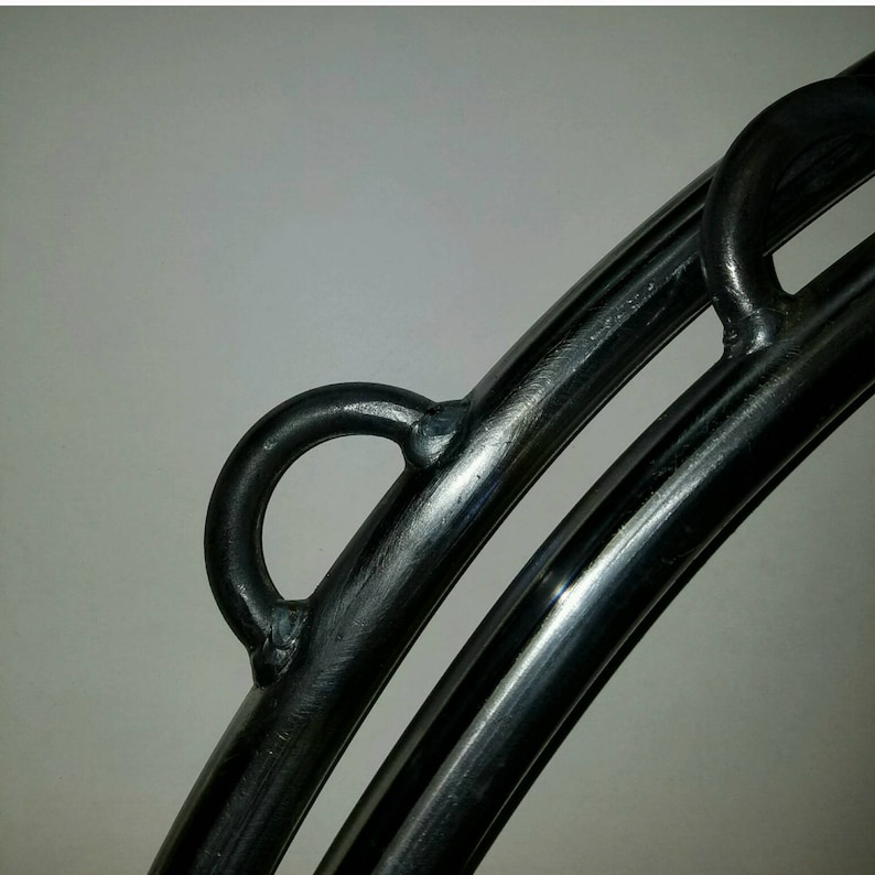 May include: Close-up of a black metal hoop with two welded loops. The hoop is made of thick, round metal and has a smooth, polished finish.