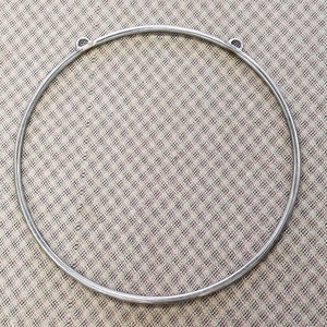 May include: A silver metal hoop with two small loops on the top. The hoop is lying flat on a patterned fabric.