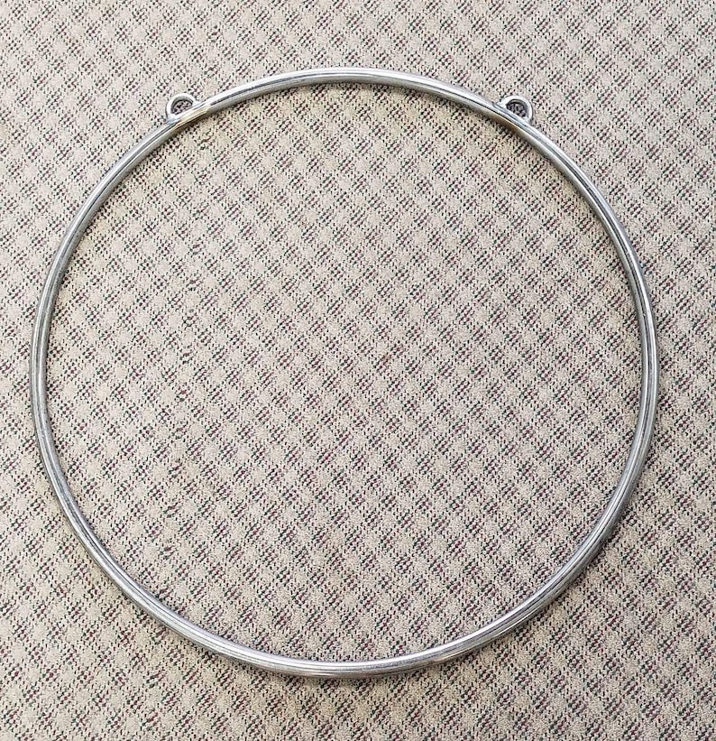 May include: A silver metal hoop with two small loops on the top. The hoop is lying flat on a patterned fabric.