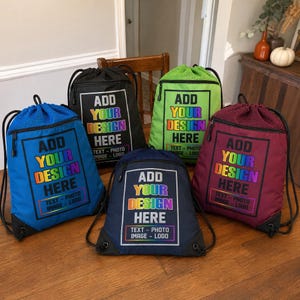 May include: Five drawstring backpacks in blue, black, lime green, navy, and maroon. Each bag features a front zippered pocket and a rectangular graphic with the text ADD YOUR DESIGN HERE, TEXT - PHOTO IMAGE - LOGO in a rainbow gradient font.