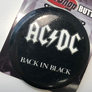 以下が含まれることがあります： AC/DCのロゴと「Back in Black」の文字が書かれた黒と白のボタン。
