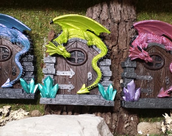 Puede incluir: Tres puertas de hadas en miniatura con dragones esculpidos en la parte superior. Las puertas son de madera y tienen un marco de piedra. Los dragones están pintados en azul, verde y rosa.