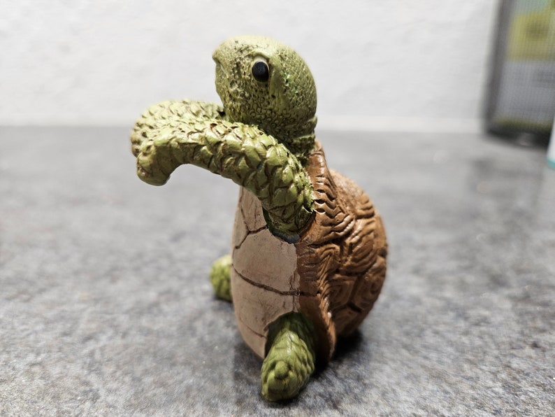 May include: A ceramic turtle figurine with a detailed, textured shell in shades of brown and green. The turtle's head and limbs are green, while the shell is brown with visible cracks. The figurine is posed as if it is crawling.