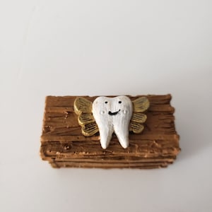 May include: A small wooden plaque with a white tooth figurine with gold wings. The tooth has a smiling face.
