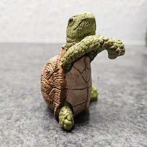 May include: A detailed figurine of a turtle with a textured shell and limbs. The turtle is primarily brown and green, with a detailed shell pattern. The figurine is posed as if it is emerging from its shell.