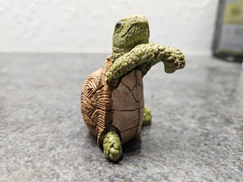 May include: A detailed figurine of a turtle with a textured shell and limbs. The turtle is primarily brown and green, with a detailed shell pattern. The figurine is posed as if it is emerging from its shell.