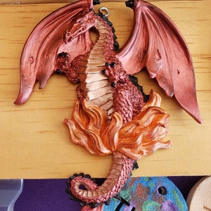 Puede incluir: Una figurita de drag&oacute;n roja y dorada con las alas extendidas, de pie sobre una base de llamas. El drag&oacute;n tiene una textura escamosa detallada y una expresi&oacute;n feroz.