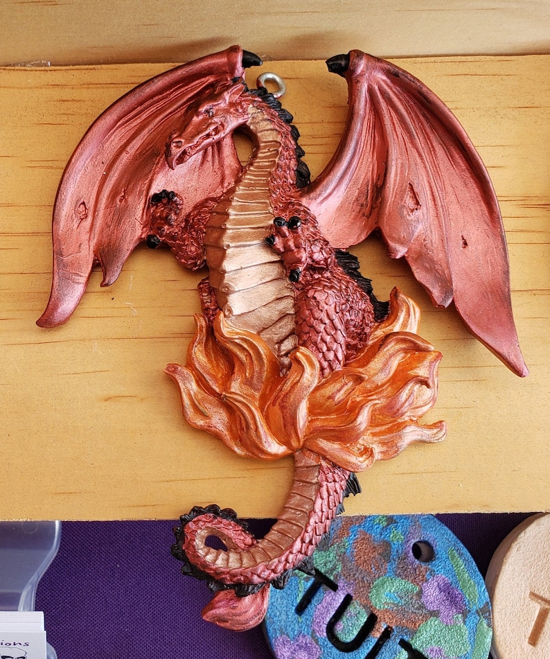 Puede incluir: Una figurita de drag&oacute;n roja y dorada con las alas extendidas, de pie sobre una base de llamas. El drag&oacute;n tiene una textura escamosa detallada y una expresi&oacute;n feroz.
