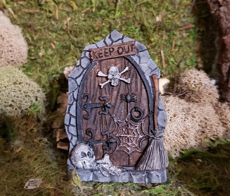 May include: A miniature stone door with a wooden door, a skull and crossbones, a spider, a cobweb, and a broom. The door has a sign that says "Keep Out".