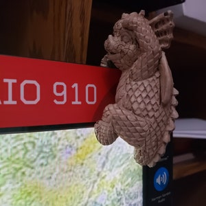 Puede incluir: Una pequeña figura de cerámica de dragón beige con una superficie texturizada y escamosa. El dragón está posado sobre una superficie roja con el texto "IO 910" impreso en ella.