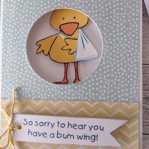 May include: A handmade greeting card with a yellow chick illustration holding a blue sling. The card has a light blue polka dot background and a banner that reads "So sorry to hear you have a bum wing!"
