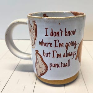 May include: White ceramic mug with a brown rim and a brown design of melting clocks. The mug has the text "I don't know where I'm going... but I'm always punctual!" printed on it.