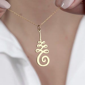 May include: A gold chain necklace with a pendant featuring a stylized symbol. The symbol is a stylized tree of life design.