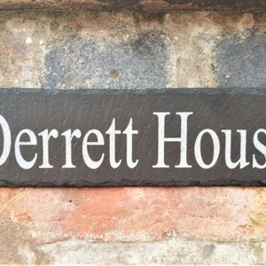 May include: A black slate house sign with white lettering that reads "Derrett House".
