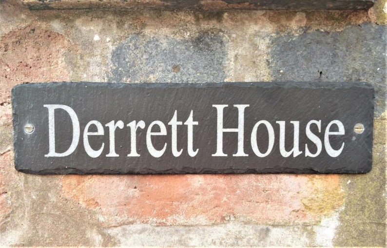 May include: A black slate house sign with white lettering that reads "Derrett House".