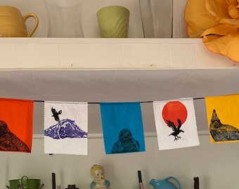 May include: A colorful fabric banner with black crow silhouettes and abstract designs. The banner is strung up on a black cord and hangs from a white shelf.