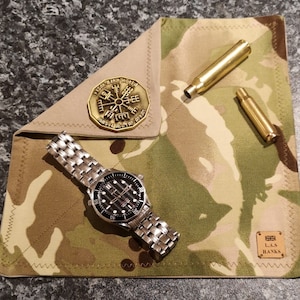 Könnte beinhalten: Eine Tasche aus Tarnstoff mit einem Kompass, einer Uhr und zwei Messingpatronenhülsen. Die Tasche hat einen braunen Lederfleck mit dem Text "L.A.S. Hanks" und einem Union-Jack-Symbol.