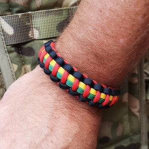 May include: A black, red and yellow paracord bracelet. The bracelet is woven with a knot pattern.