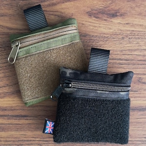 Puede incluir: Dos pequeñas bolsas con cremallera, una en camuflaje con detalles negros y la otra en camuflaje negro con una solapa de velcro negra.
