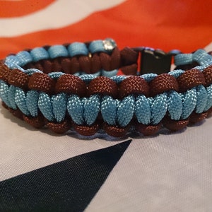 May include: A brown and light blue paracord bracelet with a black buckle closure.