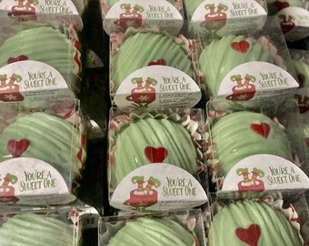 Może przedstawiać: Układ indywidualnie zapakowanych zielonych słodyczy, każdy z czerwonym sercem i etykietą z napisem "You're a Sweet One". Słodycze znajdują się w przezroczystych plastikowych pojemnikach, co sugeruje prezent lub deser.