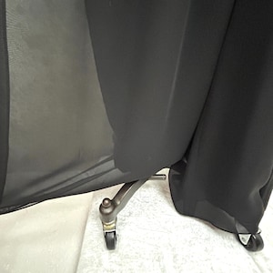 Puede incluir: Tela negra drapeada sobre un soporte met&aacute;lico con peque&ntilde;as ruedas. La tela parece transparente en algunas zonas, creando un contraste entre la luz y la sombra. El soporte tiene una est&eacute;tica vintage.