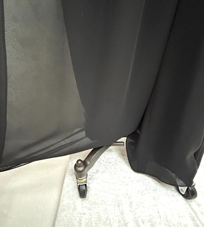 Puede incluir: Tela negra drapeada sobre un soporte met&aacute;lico con peque&ntilde;as ruedas. La tela parece transparente en algunas zonas, creando un contraste entre la luz y la sombra. El soporte tiene una est&eacute;tica vintage.