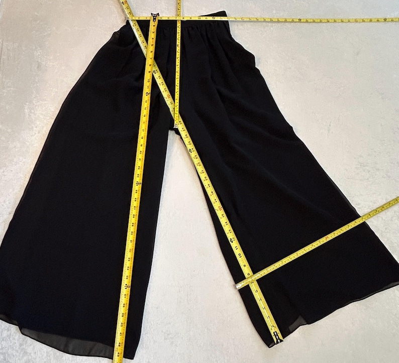 Puede incluir: Pantalones negros de pierna ancha con cintura el&aacute;stica. Una cinta m&eacute;trica amarilla se coloca sobre los pantalones para mostrar las medidas. Los pantalones est&aacute;n hechos de un material ligero.